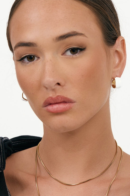Close-up of a woman wearing gold earrings and a necklace against a white background