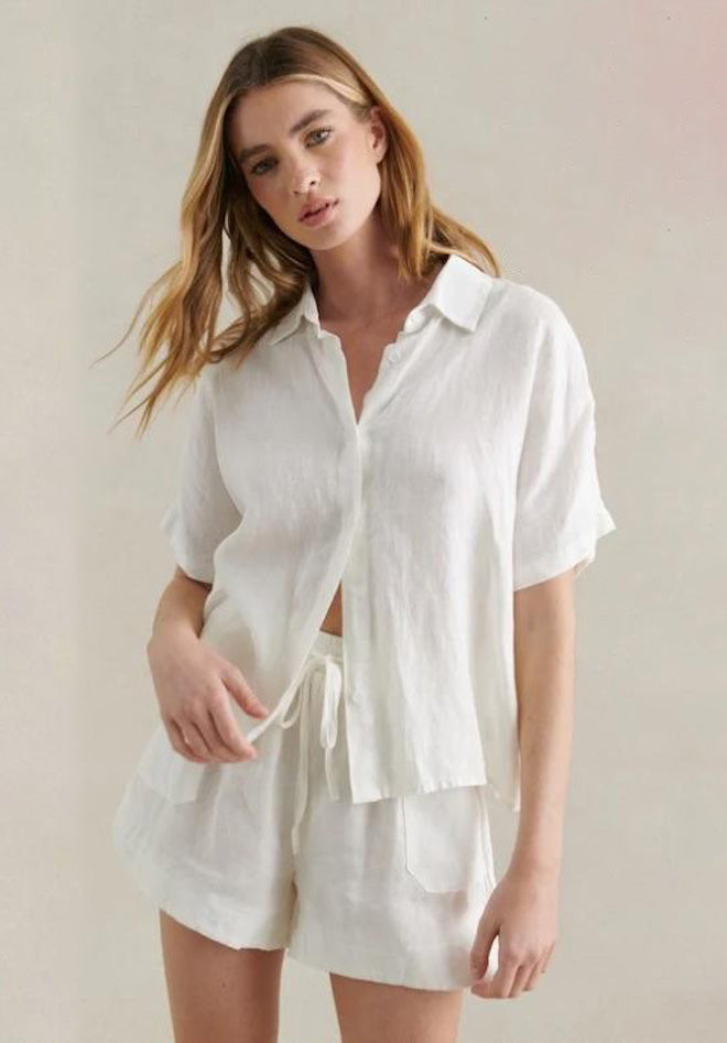 Woman wearing a white linen shirt and shorts set against a neutral background