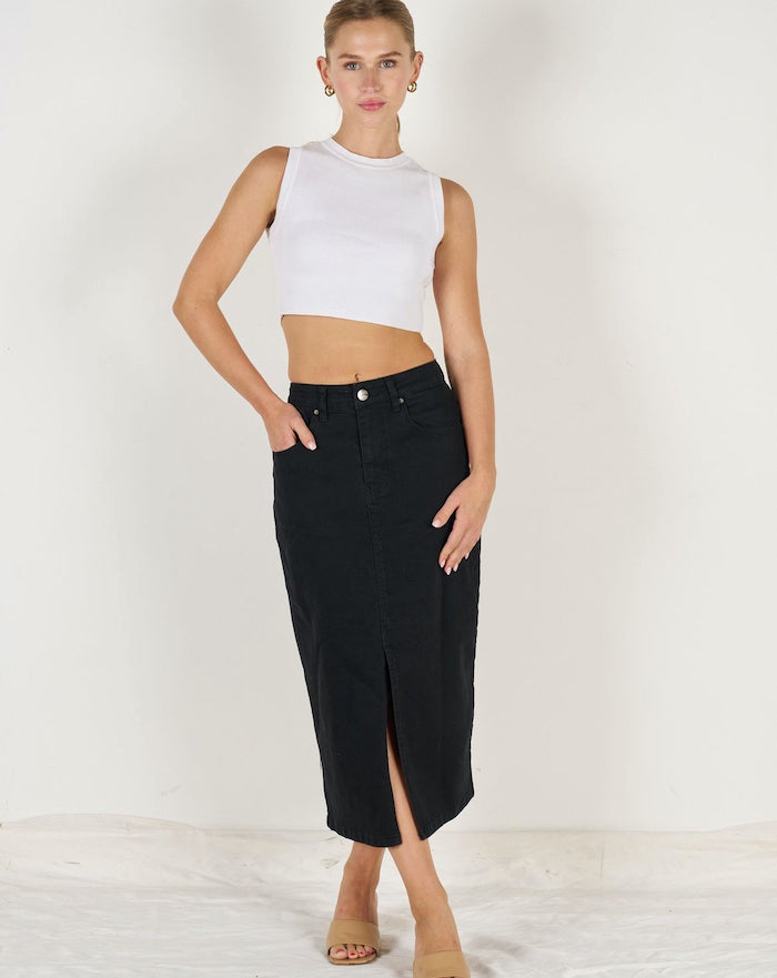 A woman standing, wearing a white sleeveless top and a black denim skirt.