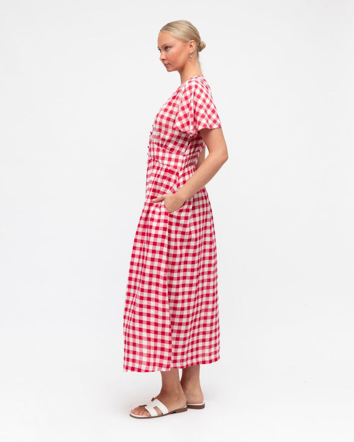 A woman standing and facing to the side, wearing a red and white checkered dress with a V-neckline and three-quarter sleeves.