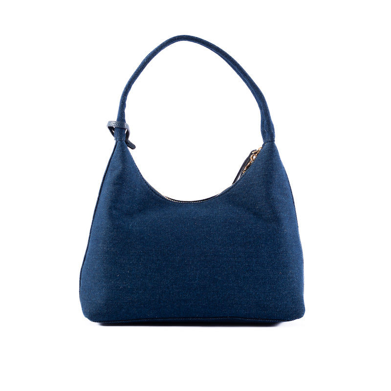 A woman smiling and posing with a blue denim handbag over her shoulder, with the brand tag visible.