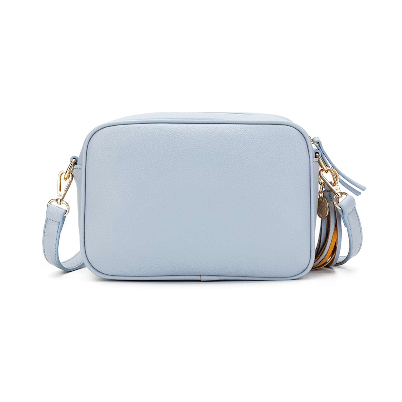 A blue chambray crossbody bag with three adjustable straps, a tassel detail, and a brushed gold hardware closure.