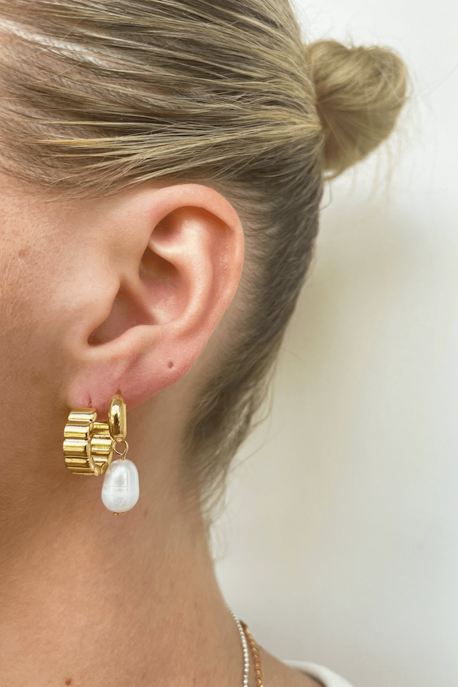 A pair of silver-colored hoop earrings with fresh water pearl adornments on a marble surface.