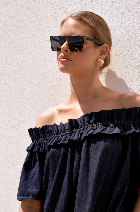 Woman wearing black sunglasses and a black off-shoulder top against a light background