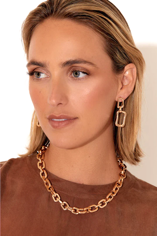 Woman wearing a gold chain necklace and earrings against a neutral background