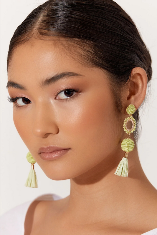 Woman wearing green tassel earrings against a white background
