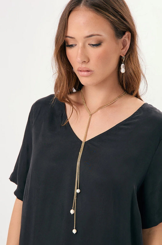 Woman wearing a black top and gold necklace with white beads on a white background