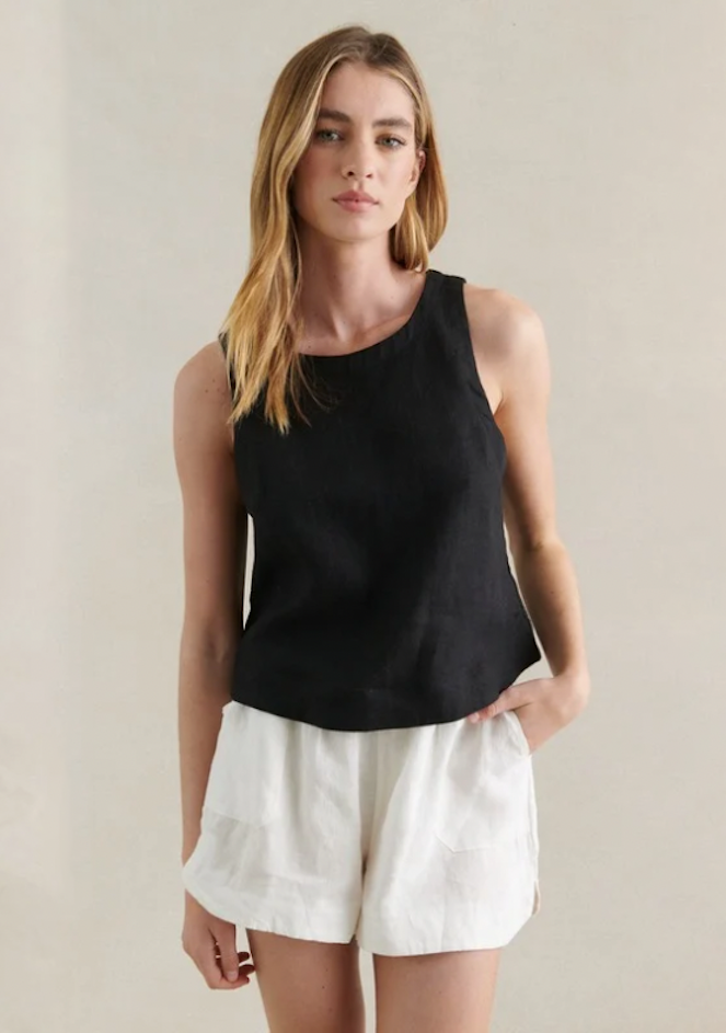 Woman wearing a black sleeveless top and white shorts against a neutral background