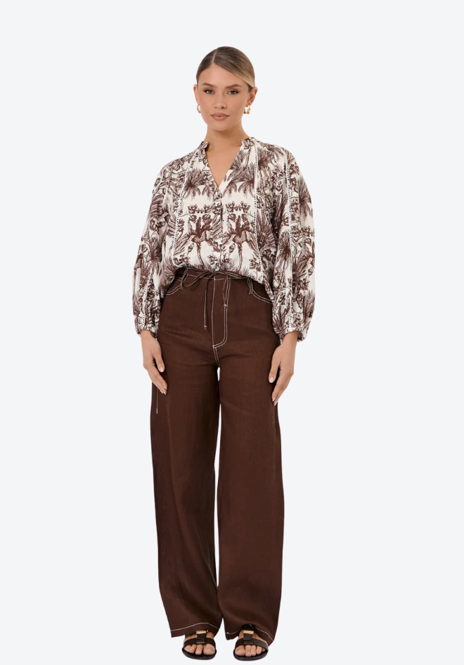 Woman wearing a patterned blouse and brown pants on a white background