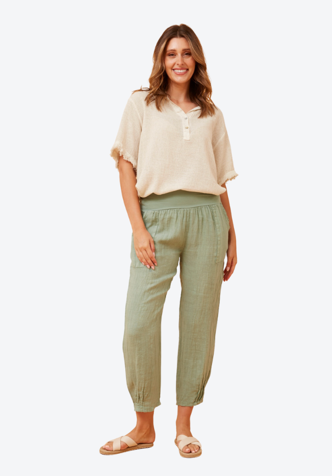 Woman wearing a beige top and green pants on a white background