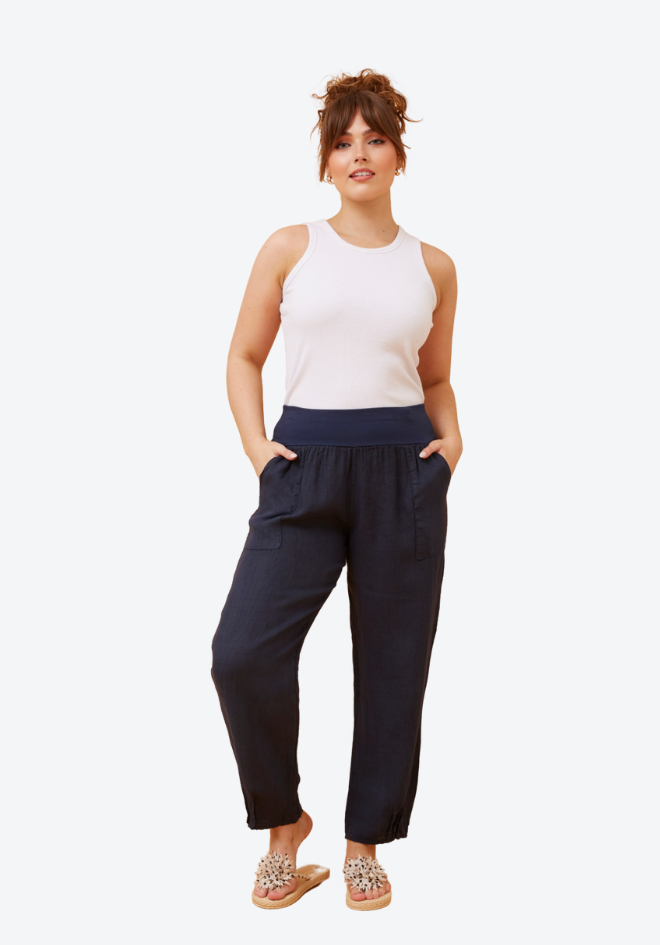 Woman wearing a white sleeveless top and navy pants on a white background