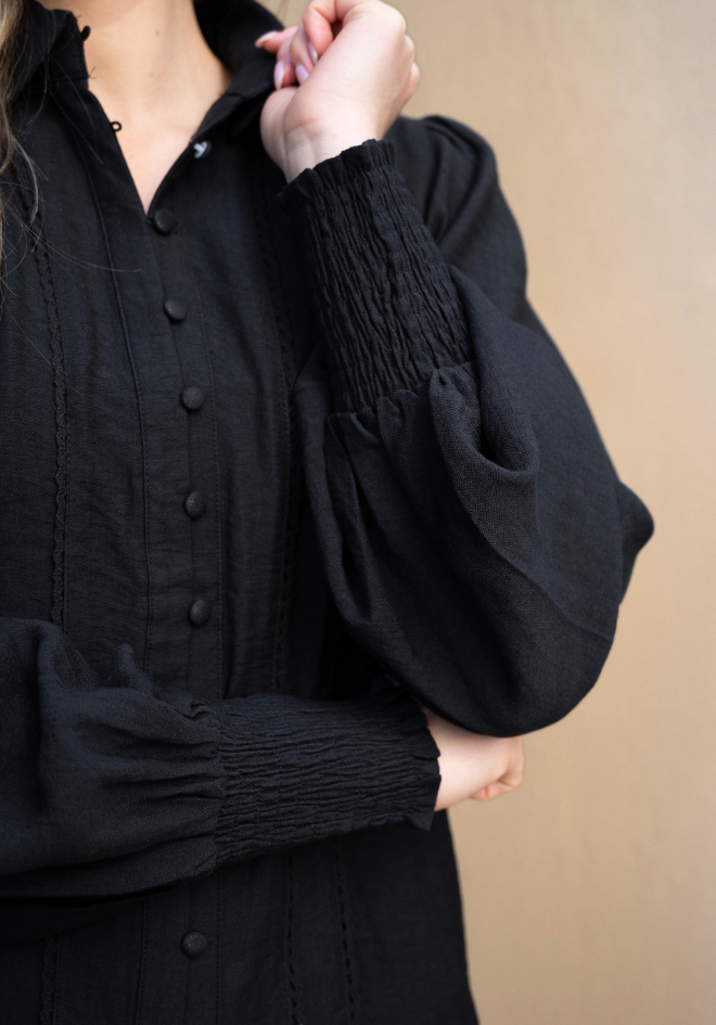 Person wearing a black button-up shirt with puffed sleeves against a beige background