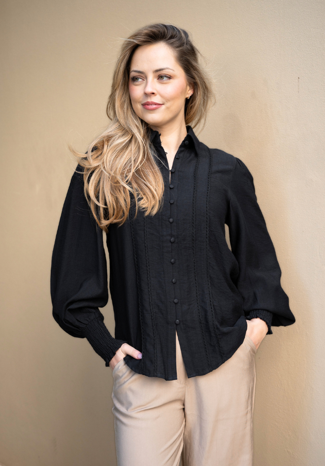 Woman wearing a black blouse and beige pants against a beige background