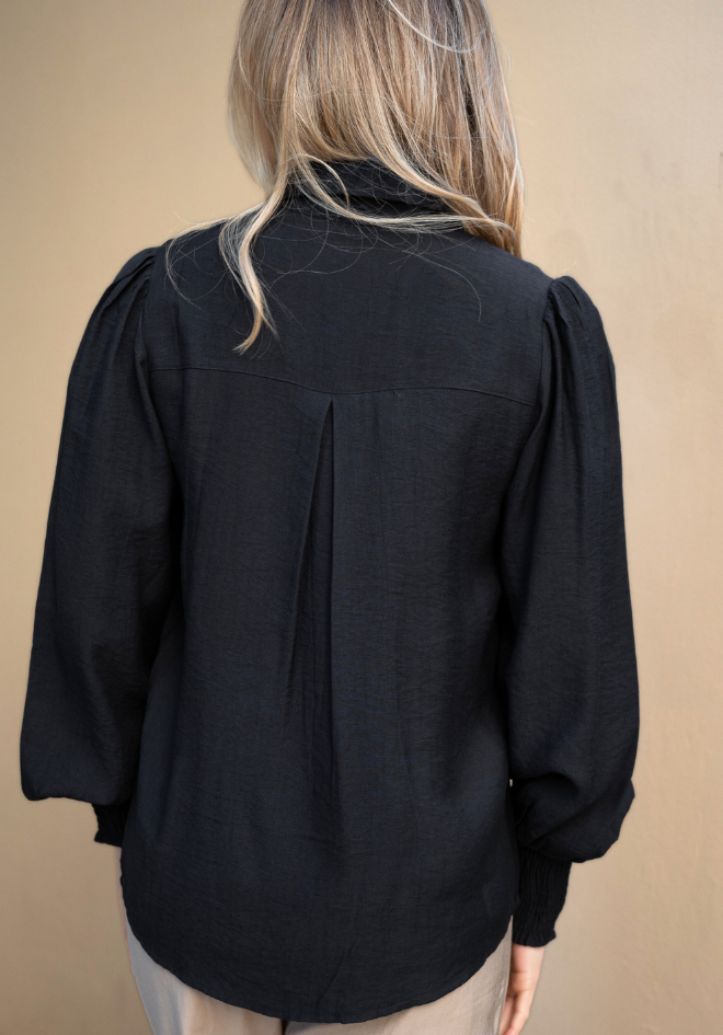 Black blouse with puffed sleeves worn by a person on a beige background