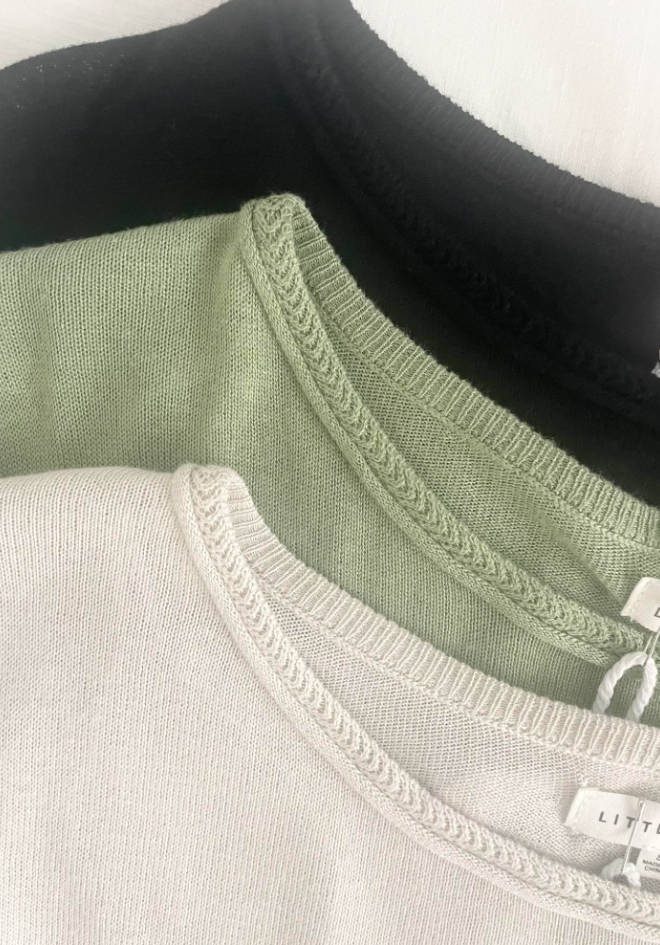 Close-up of three shirts in black, green, and white with visible labels.