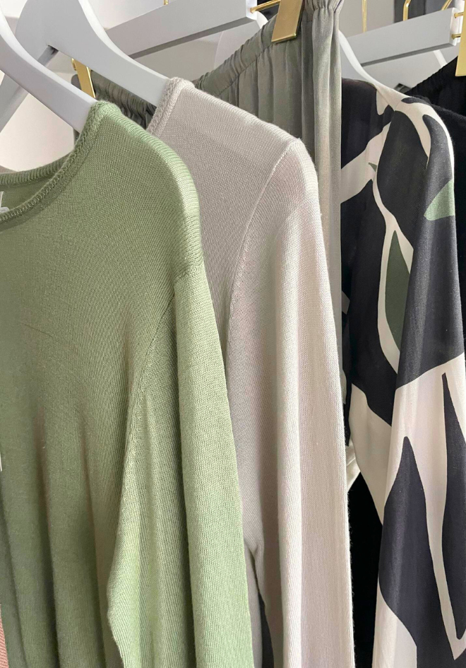 Collection of sweaters hanging on a rack with a focus on green, beige, and patterned designs.