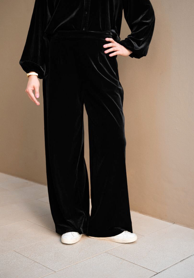 Person wearing a black velvet outfit with wide-leg pants on a neutral background