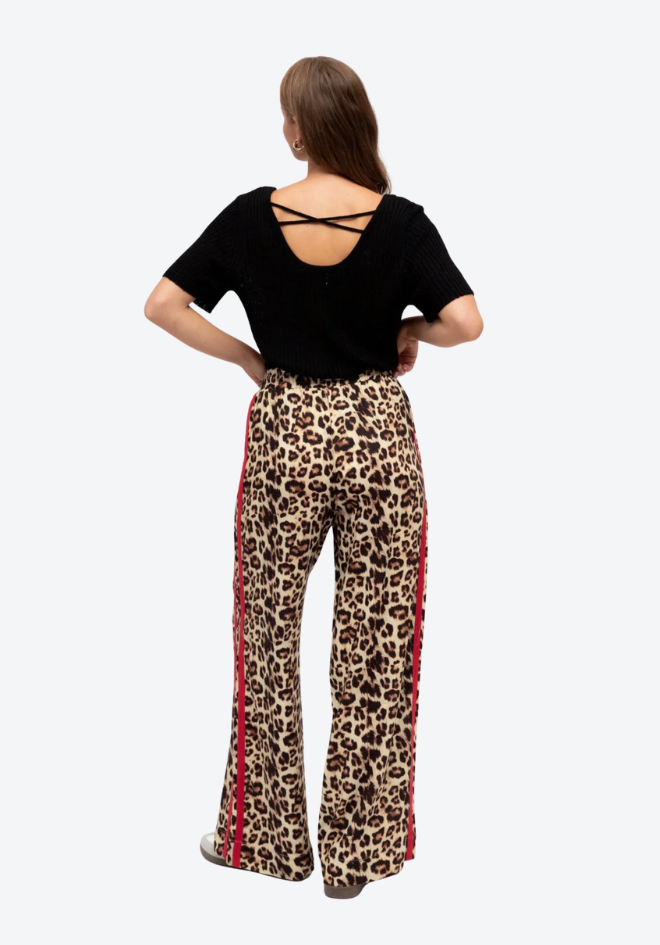 Woman wearing a black top and leopard print pants with red stripes on a white background