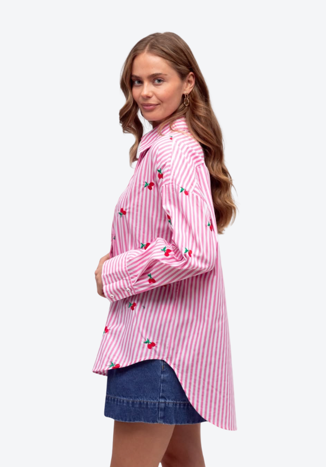 Woman wearing a pink and white striped shirt with cherry designs on a white background