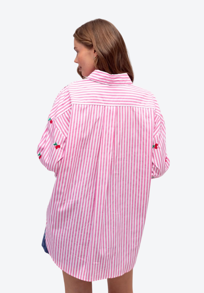 Person wearing a pink and white striped shirt with cherry designs on a white background