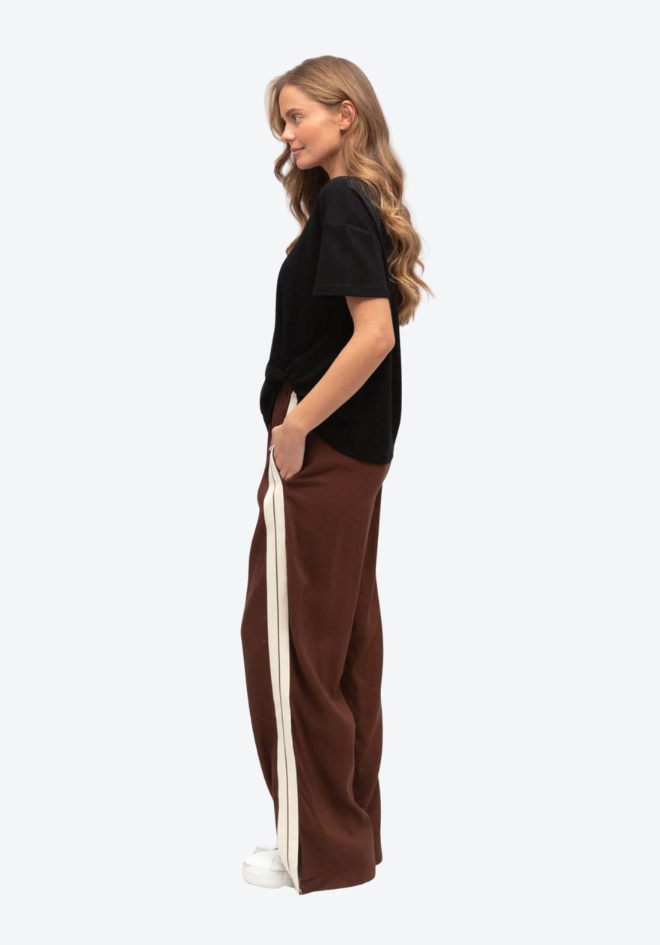 Woman wearing a black top and brown pants with a white stripe on a white background