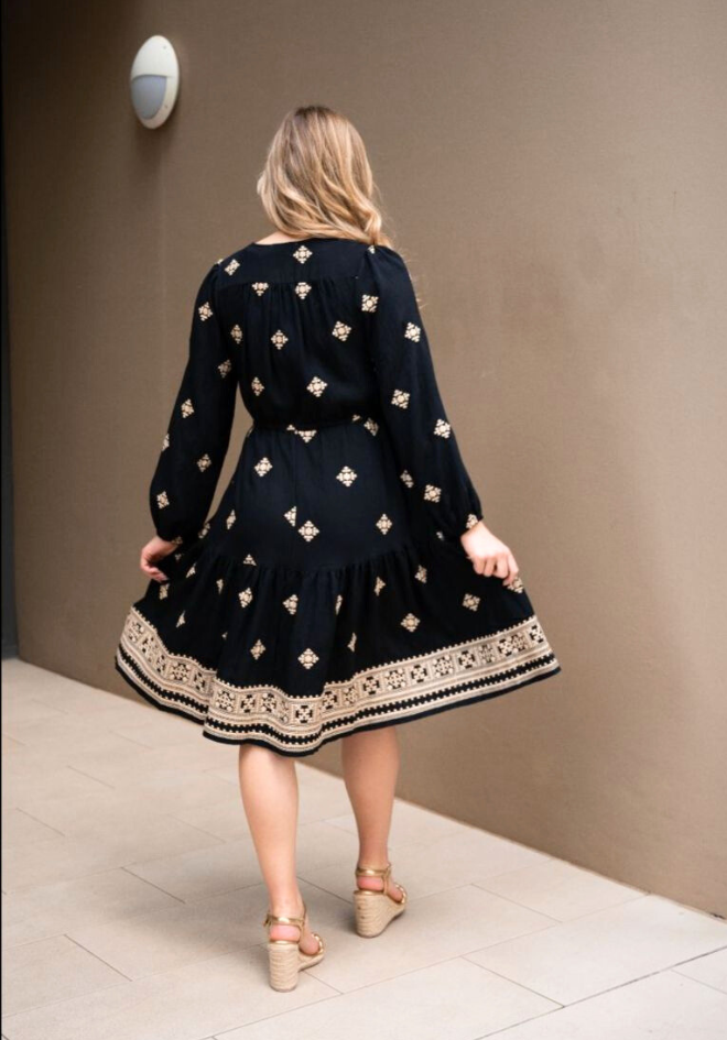 Woman wearing a black dress with white patterns in a room.