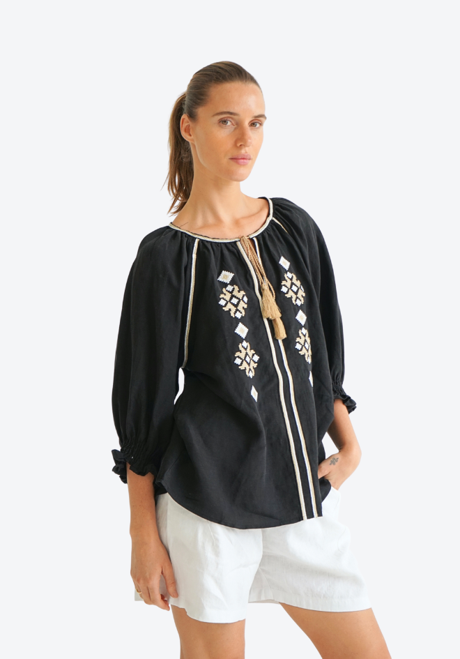 Woman wearing a black blouse with white embroidery and white shorts on a white background