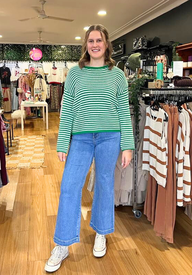 Woman wearing a green striped sweater and blue jeans standing in a clothing store.