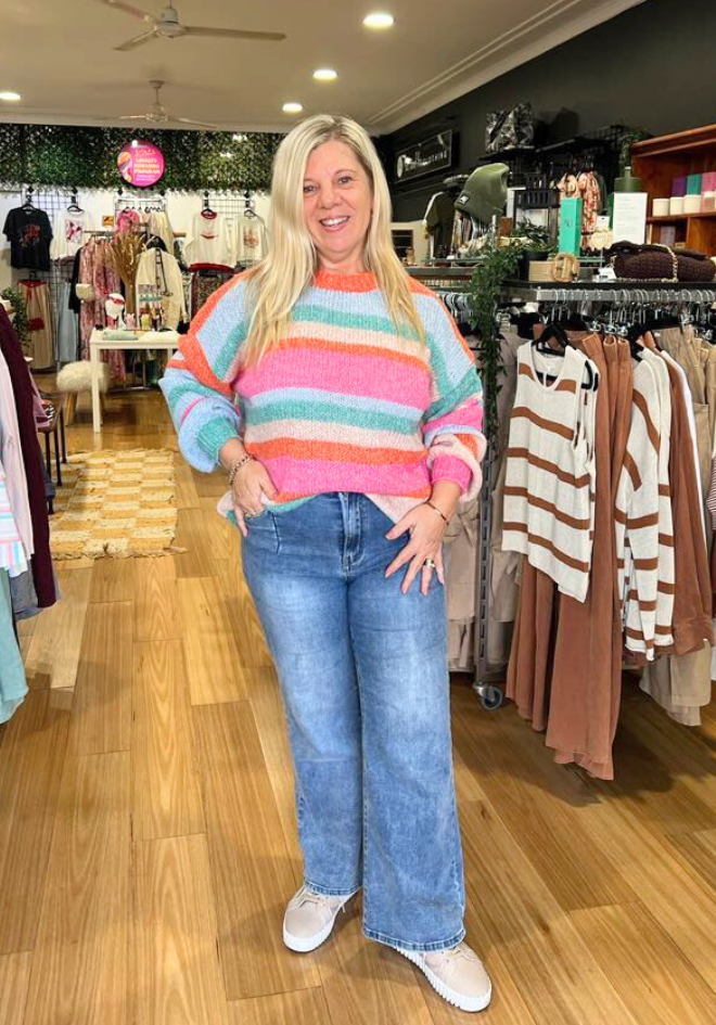 Woman wearing a colorful striped sweater and jeans in a clothing store.