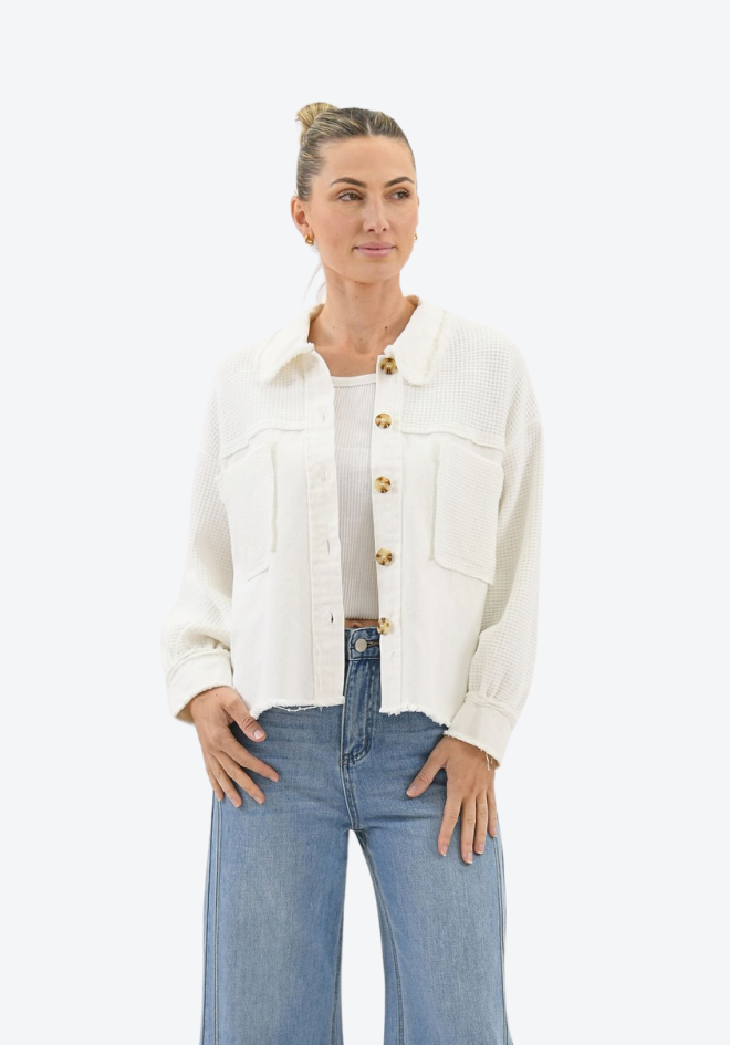 Woman wearing a white jacket with gold buttons and blue jeans on a white background