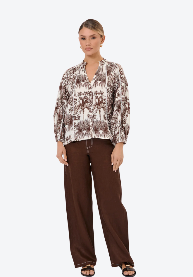 Woman wearing a patterned blouse and brown pants on a white background