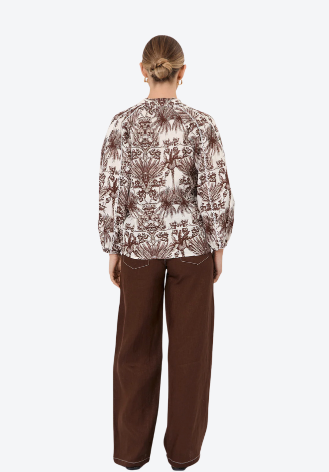 Person wearing a patterned shirt and brown pants on a white background