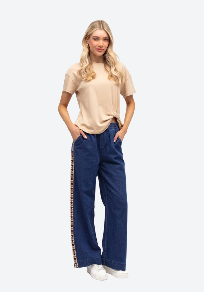 Woman wearing a beige top and blue pants with a stripe on a white background