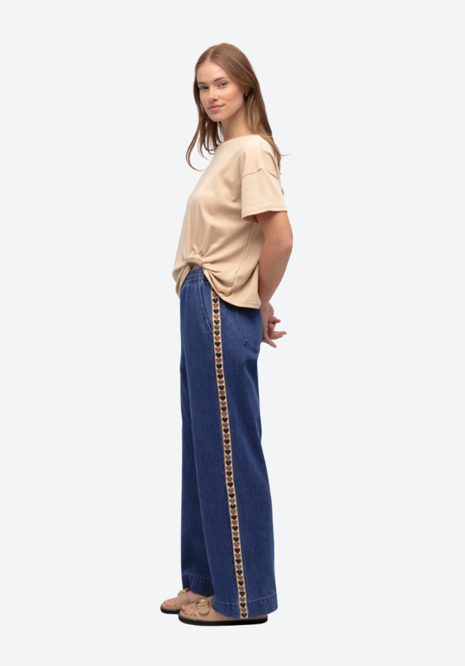 Woman wearing a beige top and blue pants with a patterned side stripe on a white background