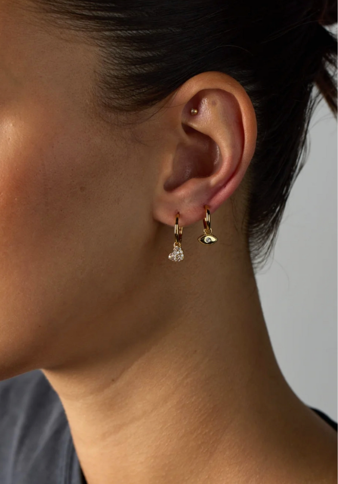 Close-up of a person wearing two earrings on a neutral background
