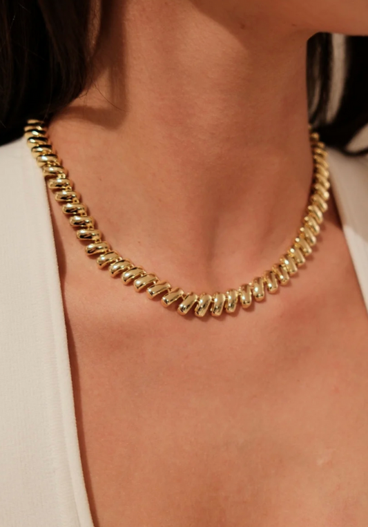 Gold chain necklace worn by a person with a neutral background