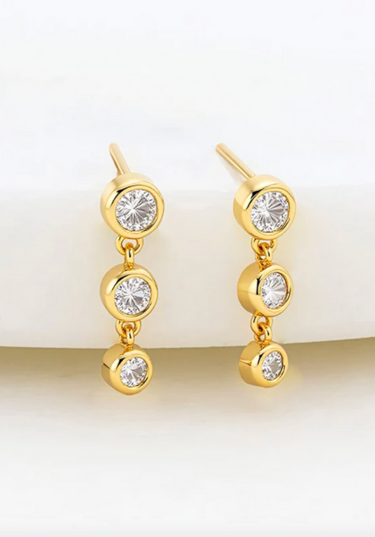 Gold earrings with clear gemstones on a gradient background