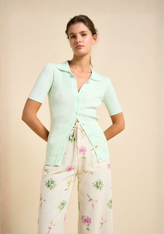 Woman wearing a light green top and floral pants against a beige background