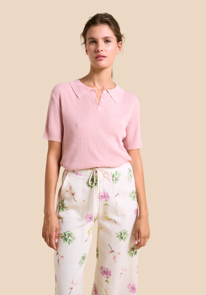 Woman wearing a pink polo shirt and floral pants on a beige background