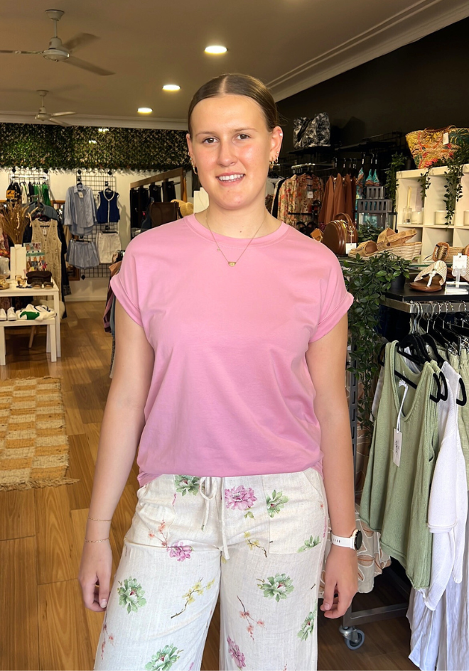 Woman wearing a pink shirt and floral pants in a clothing store.