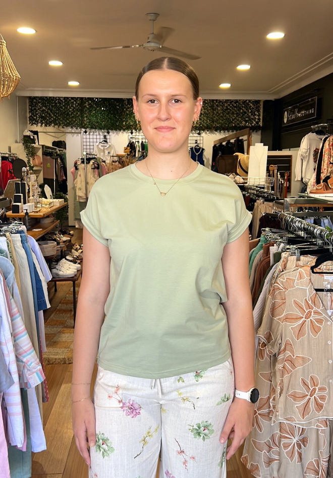 Woman wearing a light green shirt and floral pants in a clothing store.