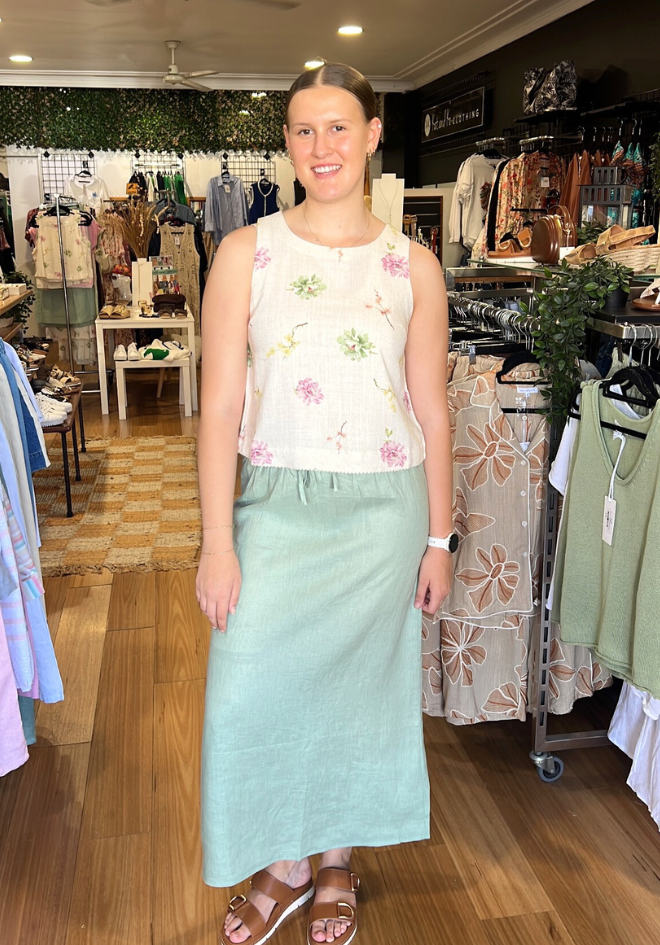 Woman in a floral top and light blue skirt standing in a clothing store.