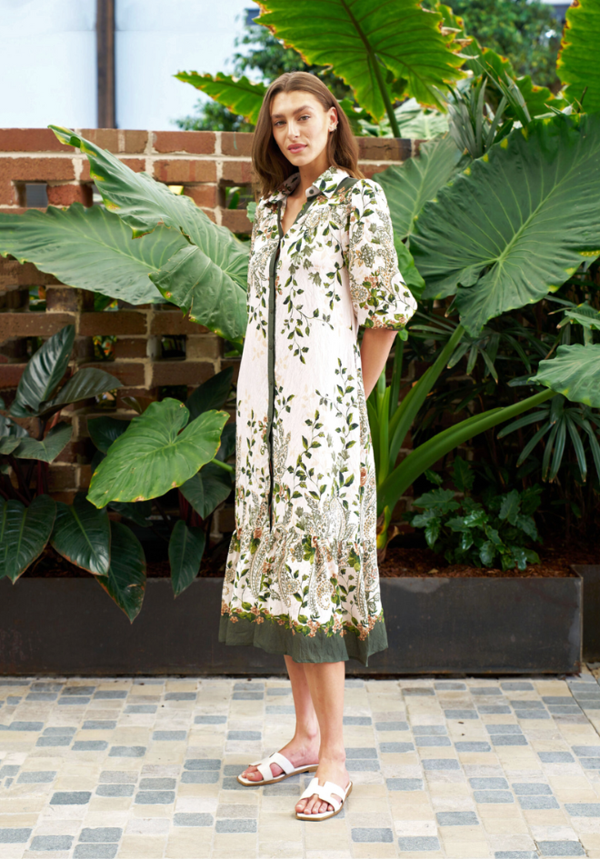 Woman in a floral dress standing in front of large green leaves