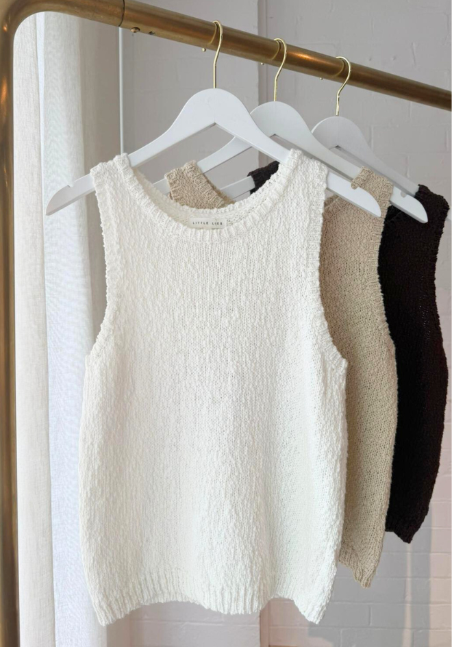 White textured sleeveless top on a hanger with other tops in the background.