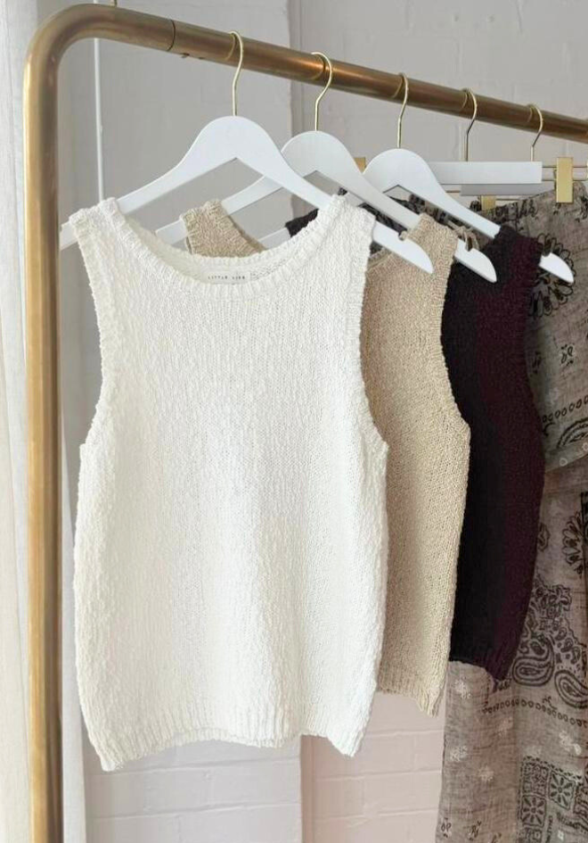 White sleeveless top on a hanger with other clothing items in the background.