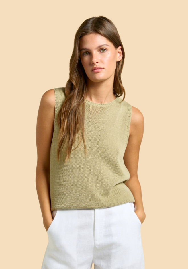 Woman wearing a green sleeveless top and white pants against a beige background