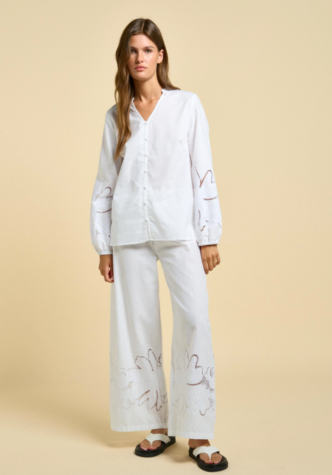 Woman wearing a white outfit with floral embroidery on a beige background