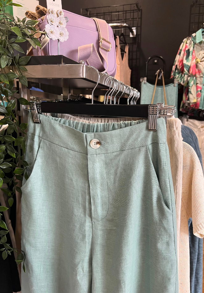 A pair of green Della Linen Pants hanging on a hanger, displaying the full length and side pocket.