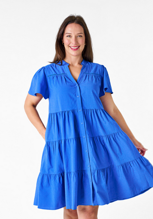 A woman wearing a knee-length blue dress with flutter sleeves, a V-neckline, and side seam pockets.