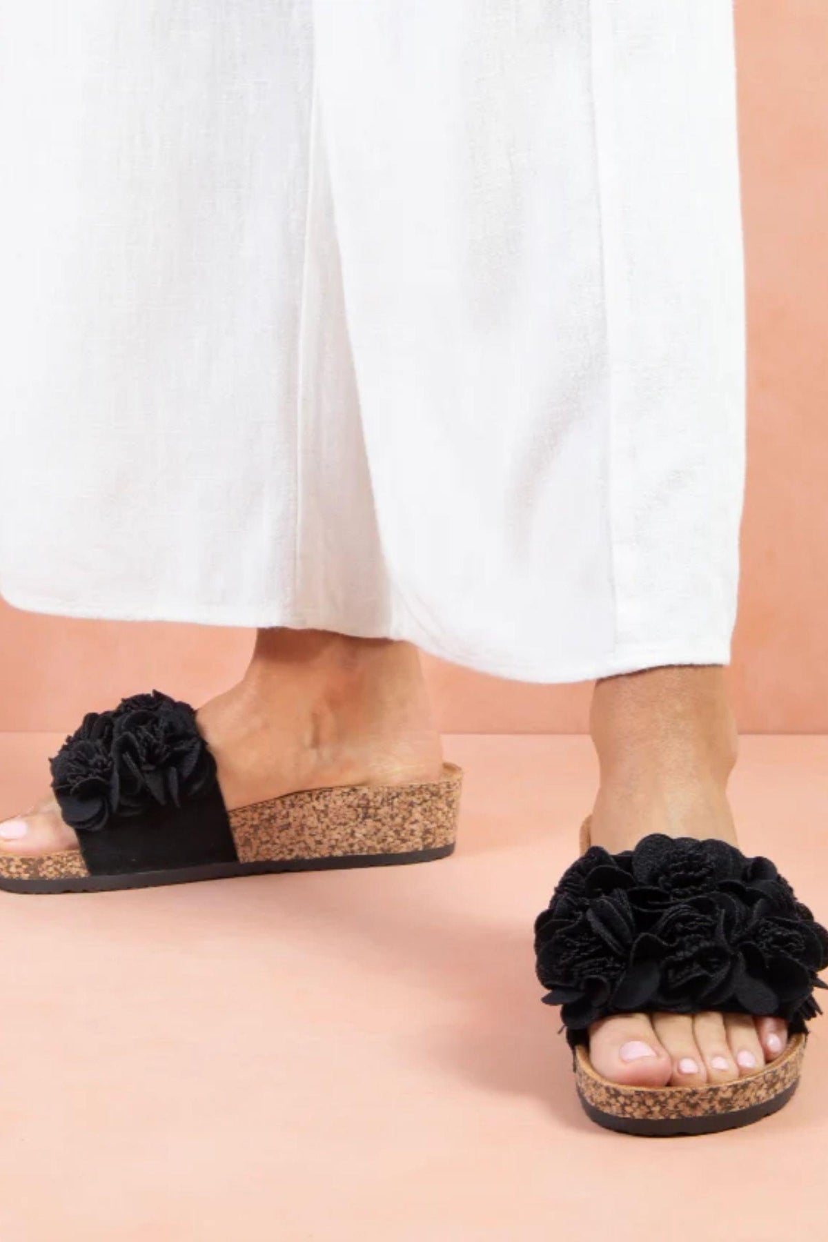 Corsage Slide in Black by Los Cabos worn on foot — close-up while walking, showing the floral detail and wedge heel